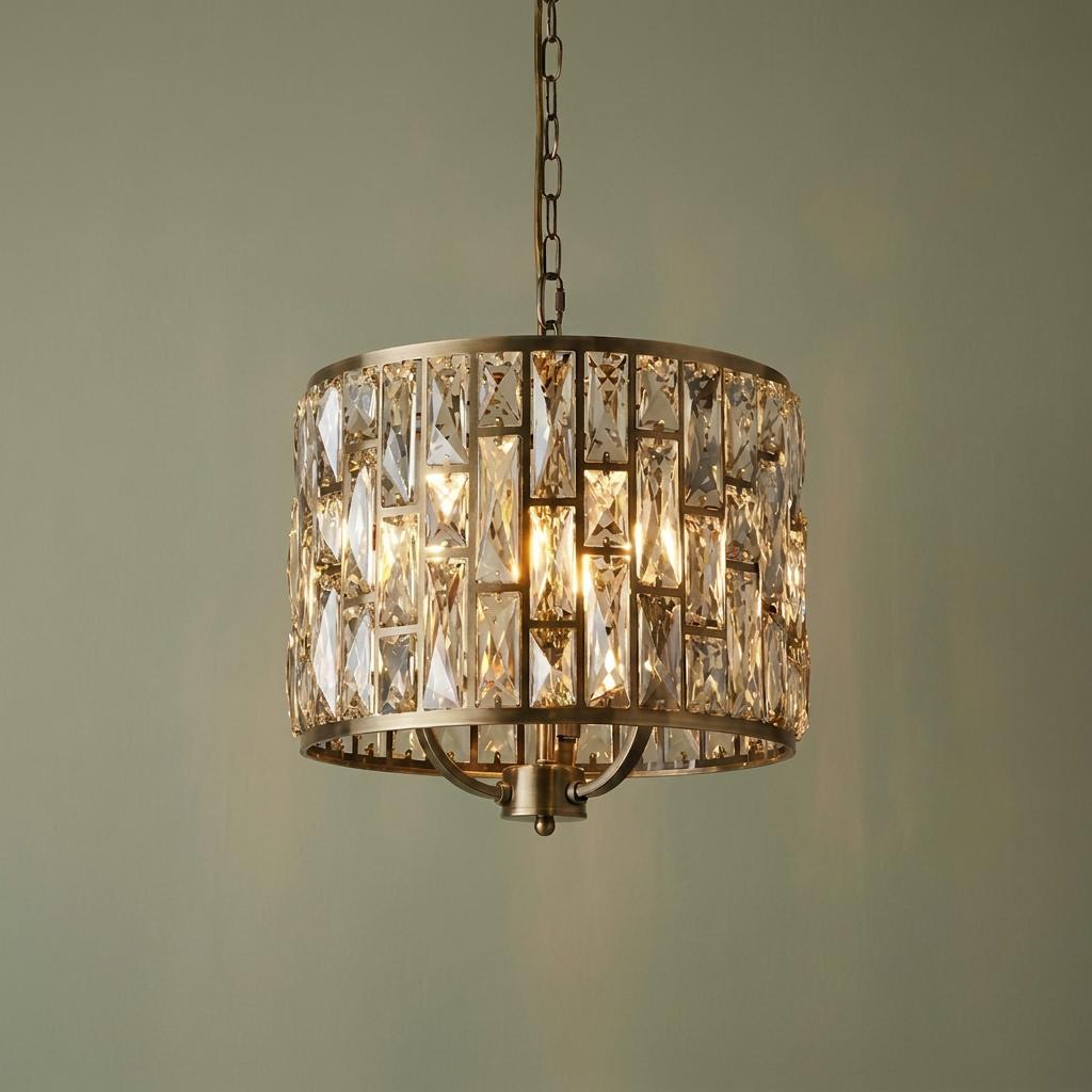 A 3-light brass drum pendant with champagne glass crystals glowing warmly against a neutral wall.
