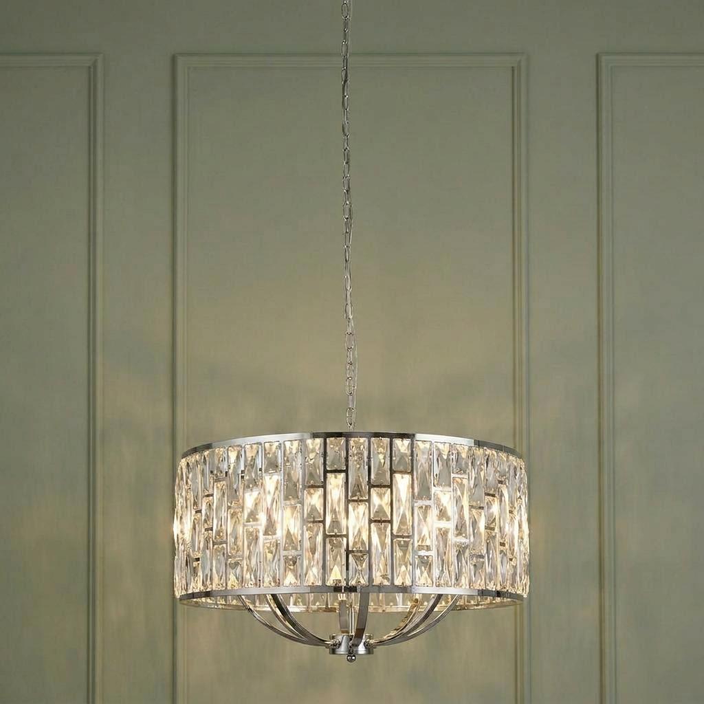 Chrome drum chandelier featuring rectangular crystal glass pieces, hanging against a sage green paneled wall.