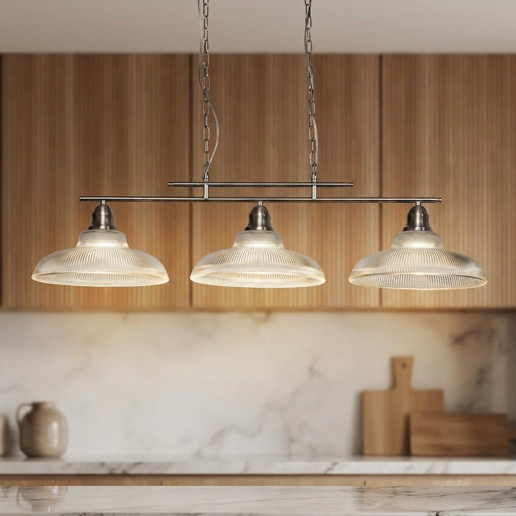 Three-light silver bar pendant with holothane glass shades hanging in a kitchen with wooden cabinets.
