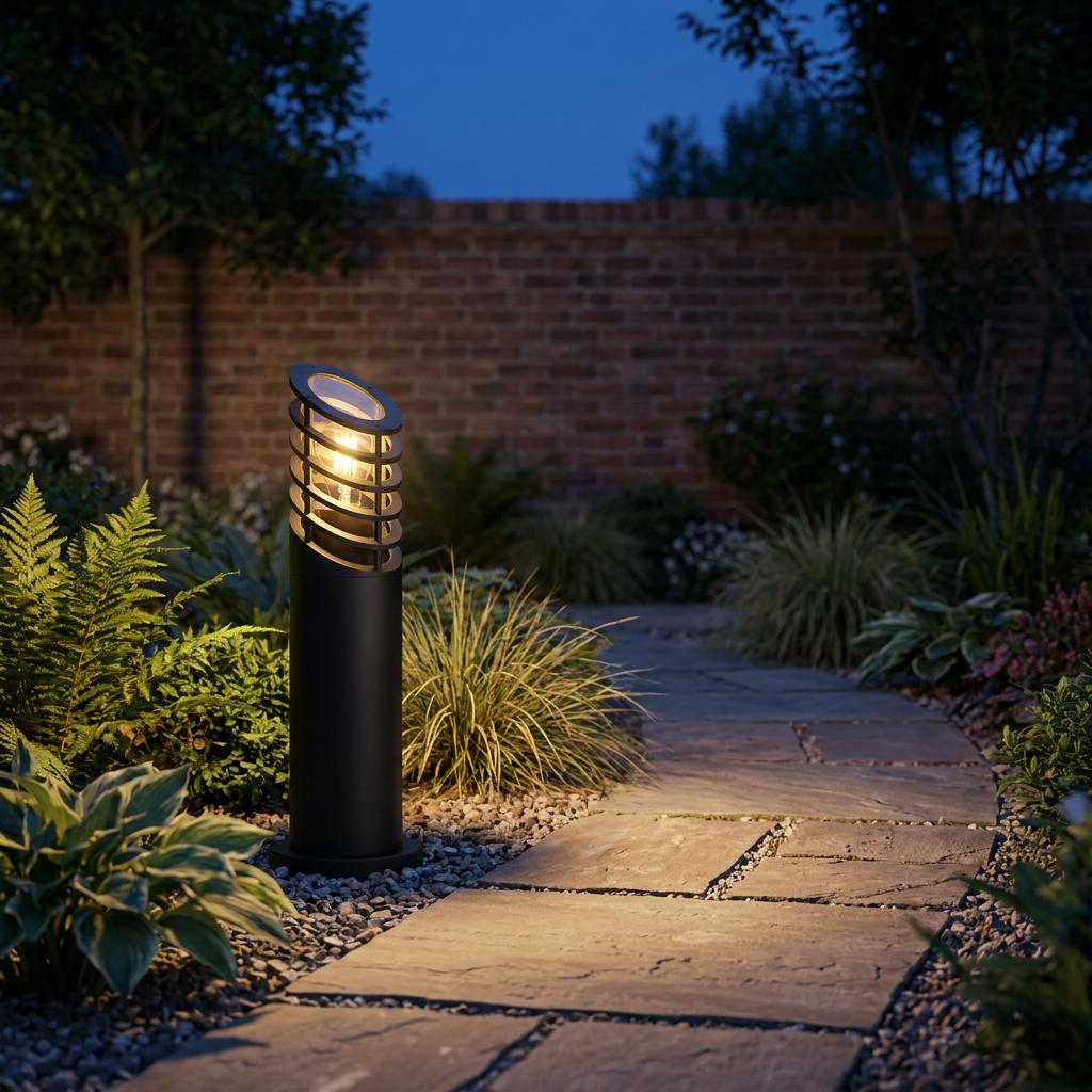 Modern black bollard light illuminating a stone garden path at night with a brick wall background.