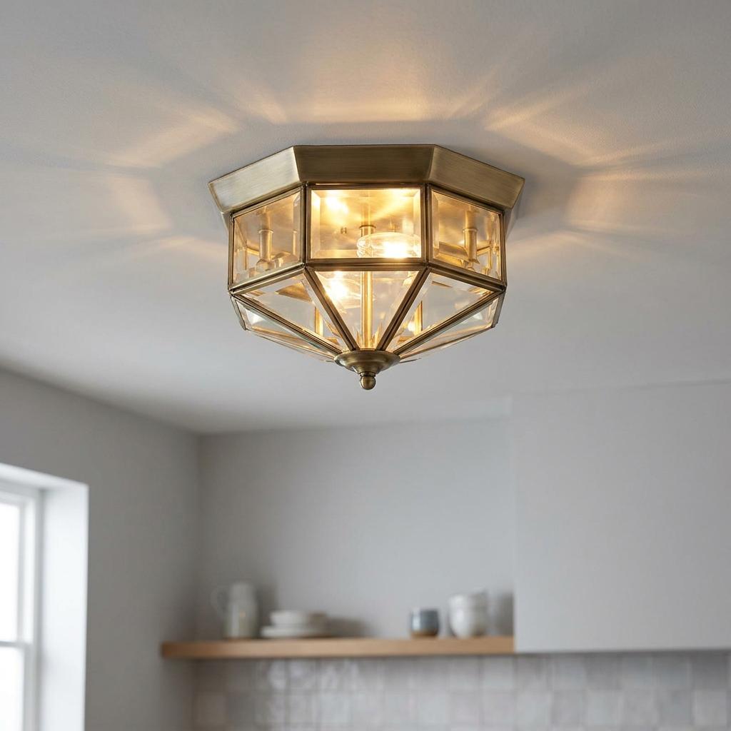 Geometric brass and clear glass flush mount ceiling light glowing with warm light on a white ceiling.