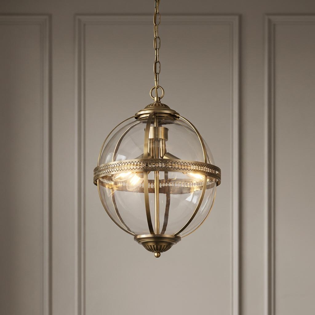 Searchlight Coronet 3-light brass and glass globe pendant hanging against a neutral paneled wall.