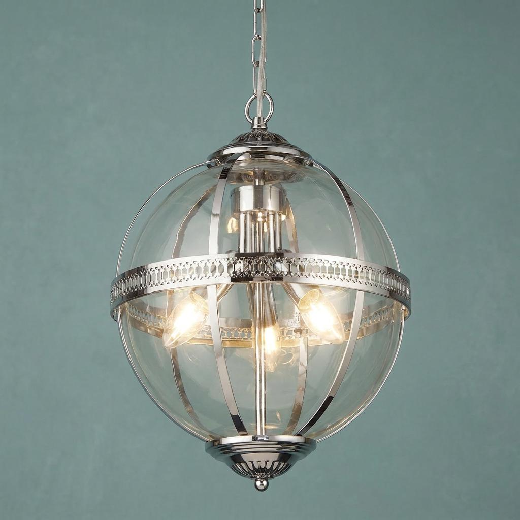 A spherical chrome and clear glass pendant light with three lit bulbs, suspended against a teal wall.