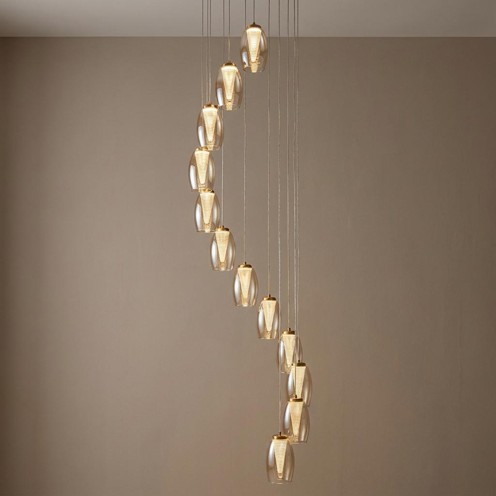 A 12-light bronze spiral pendant with champagne glass shades and glowing LED filaments against a neutral wall.