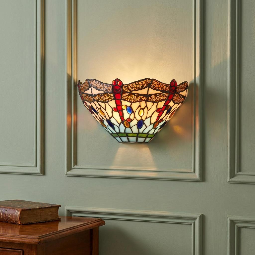 Dragonfly-patterned Tiffany wall sconce with vibrant stained glass glowing on a light green paneled wall.