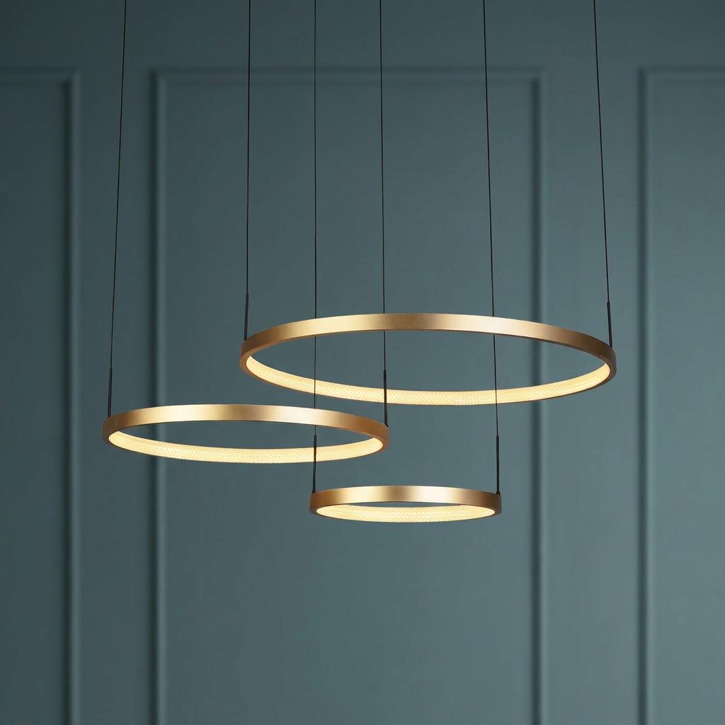 Three glowing gold circular LED rings suspended at different heights against a dark blue paneled wall.