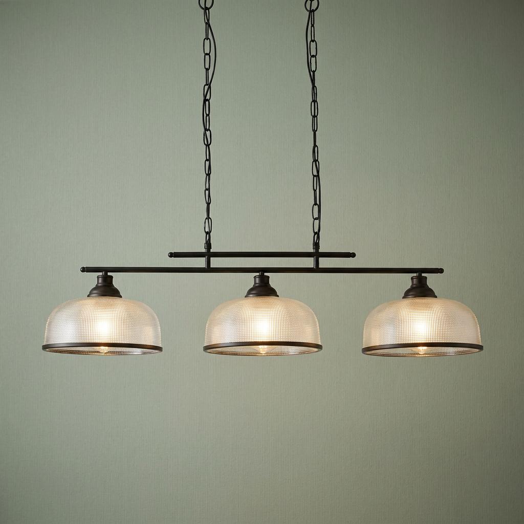 Three-light black bar pendant with holophane style glass shades hanging from two chains against a sage green wall.