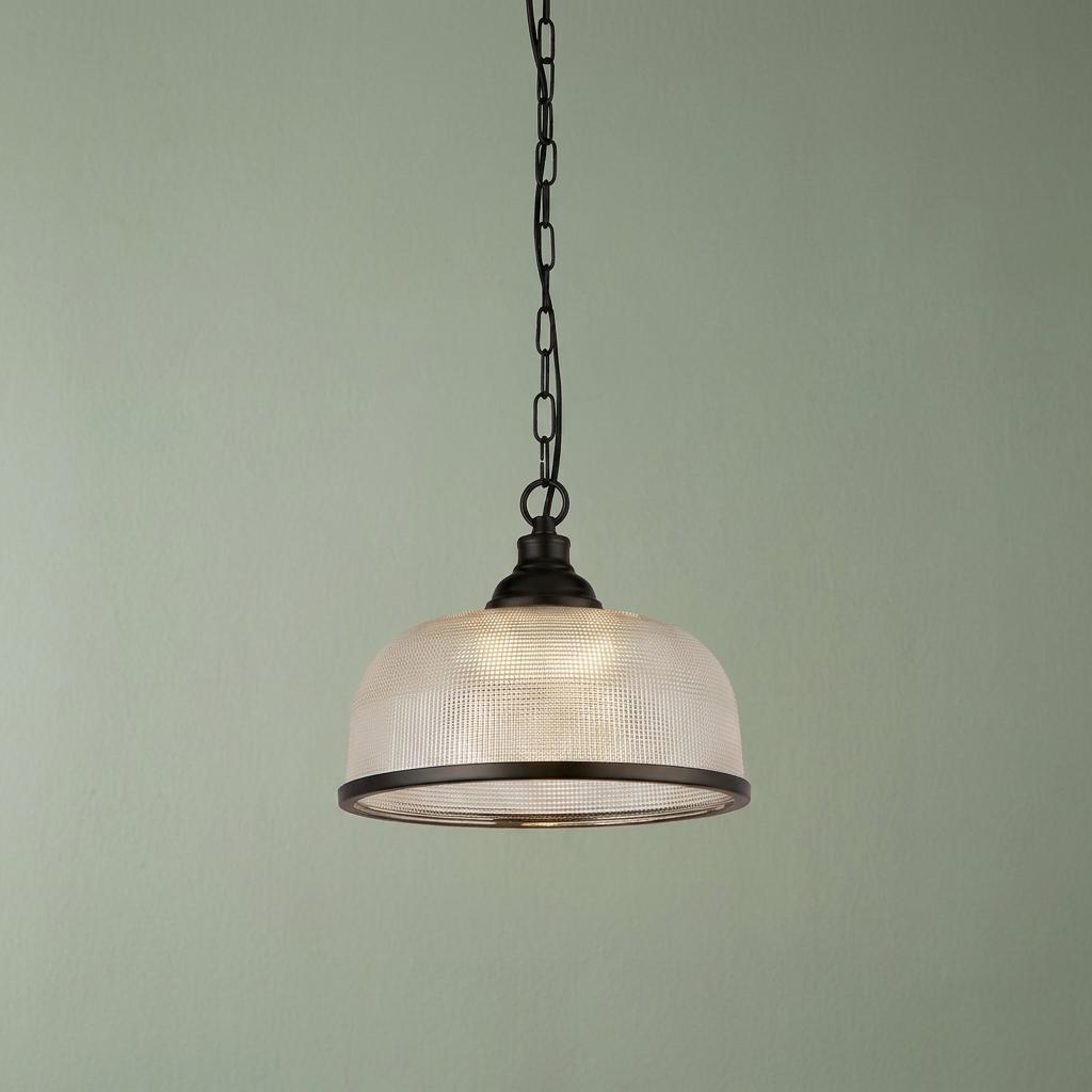 Prismatic glass dome pendant light with black trim and chain, illuminated against a light green wall.