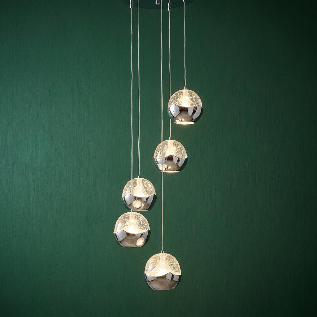 Five chrome and glass globe pendants at staggered heights against a dark green textured wall.