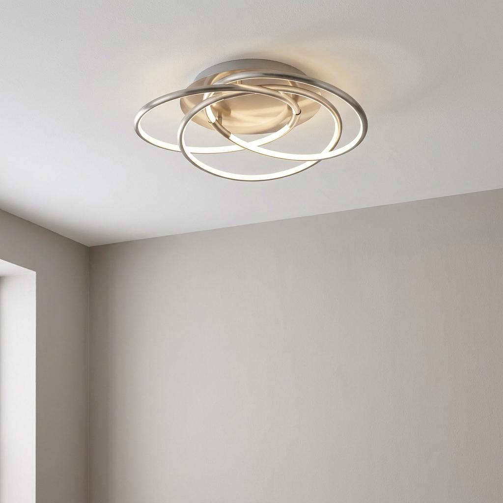 Modern satin silver ceiling light with interlocking LED rings glowing against a white ceiling.