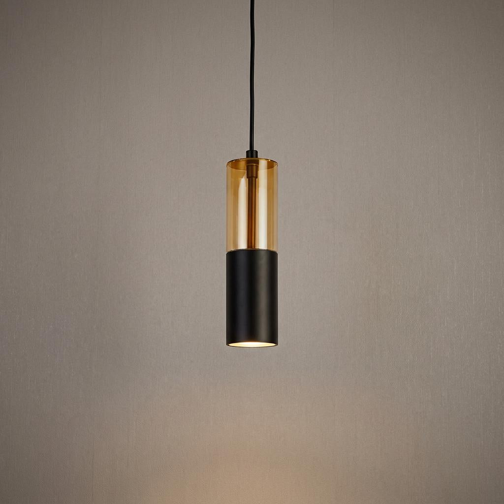 Modern cylindrical pendant light with amber glass and matte black finish suspended against a textured wall.