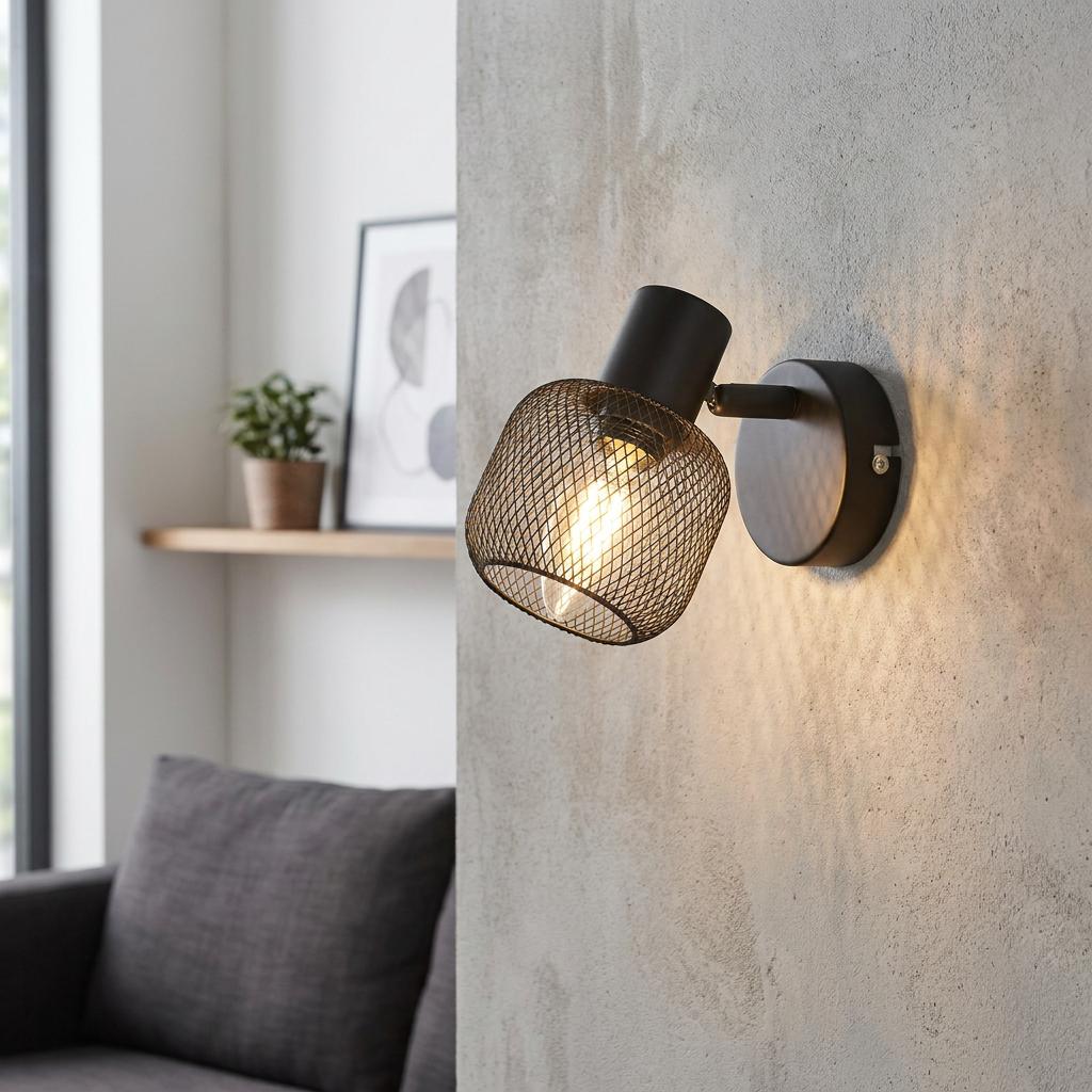 Black metal wall spotlight with a mesh cage shade lit on a textured concrete wall.