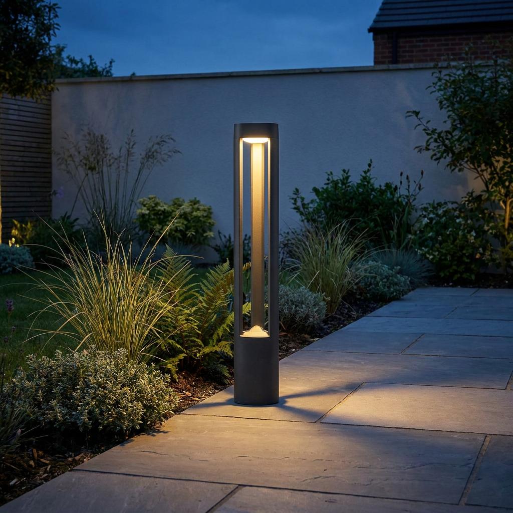 Sleek dark grey Michigan bollard light emitting a warm glow on a paved garden path at twilight.