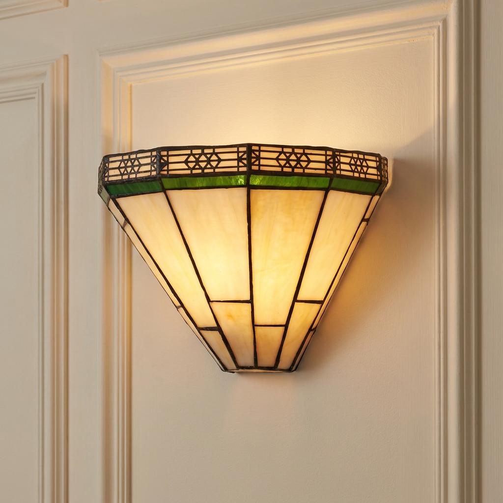 Warmly lit Tiffany wall light with cream and green stained glass panels on a white paneled wall.