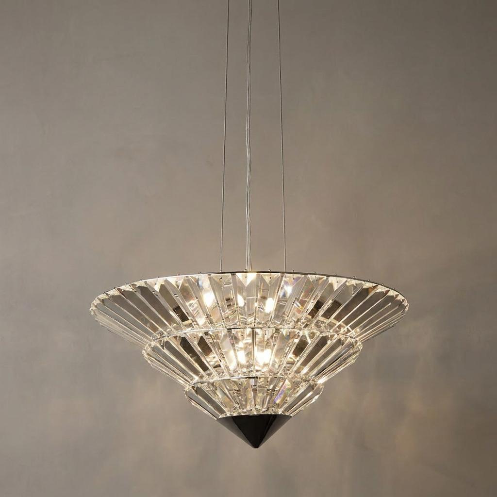 Modern tiered crystal pendant light with a cone shape, suspended by thin cables against a plain grey wall.
