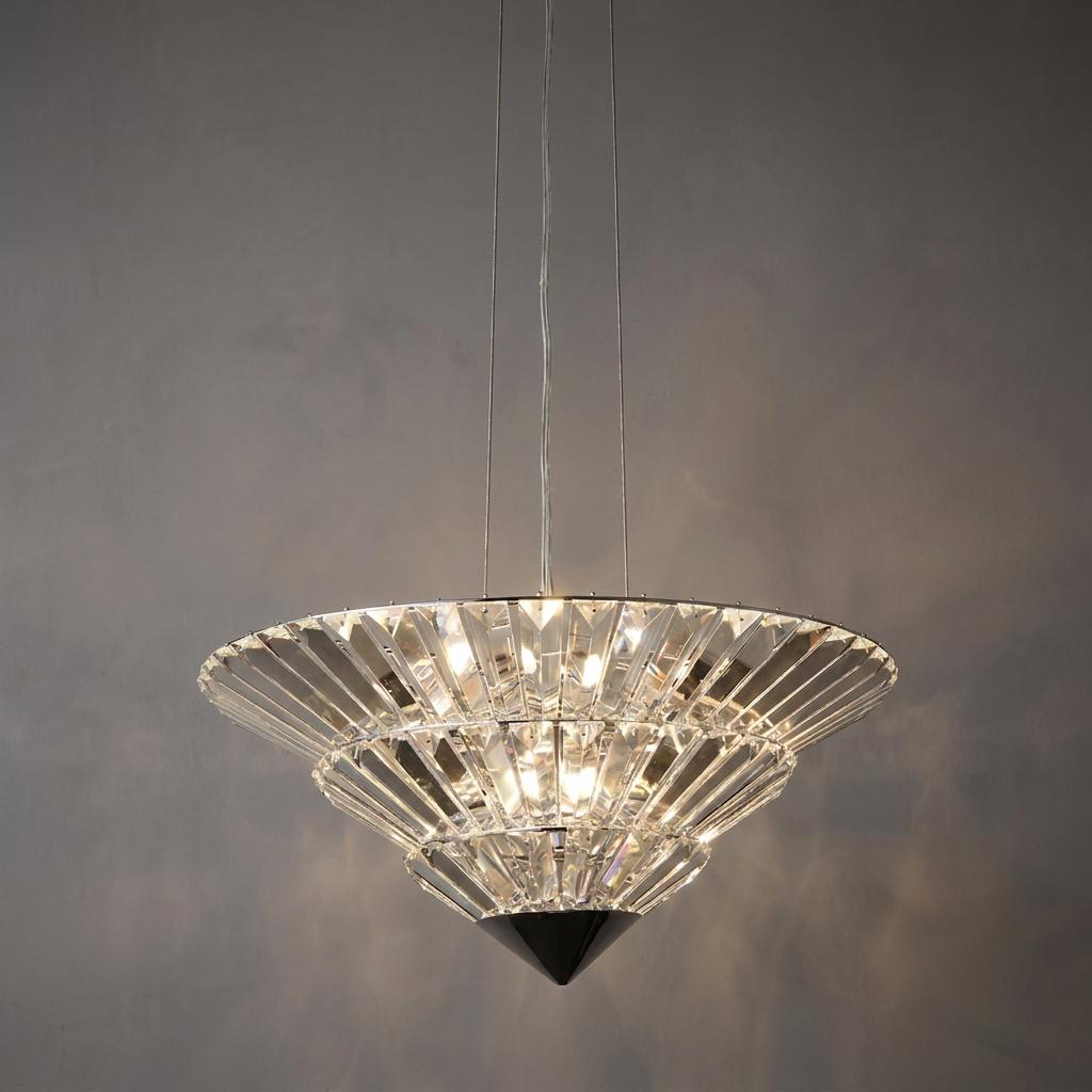 Tiered chrome and crystal pendant light with an illuminated funnel shape against a dark wall.
