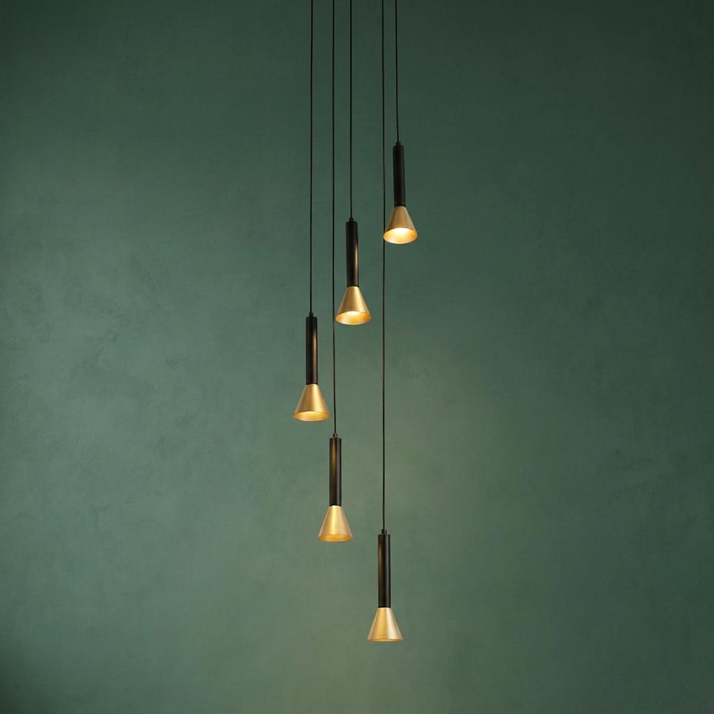 Staggered five-light black and gold pendant fixture glowing against a textured dark green wall.
