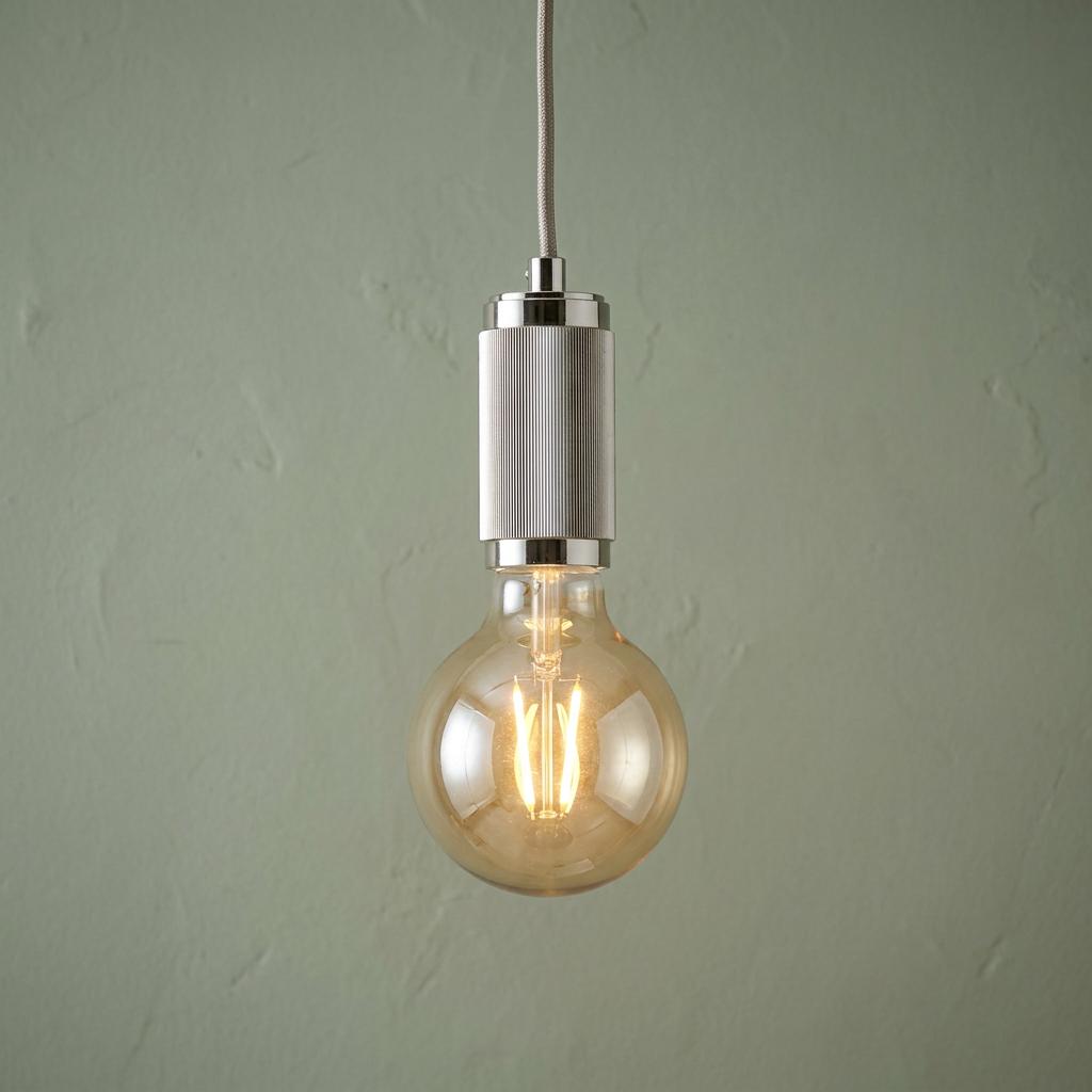 Lit spherical LED bulb on a silver knurled pendant fixture with grey braided cable against a sage wall.