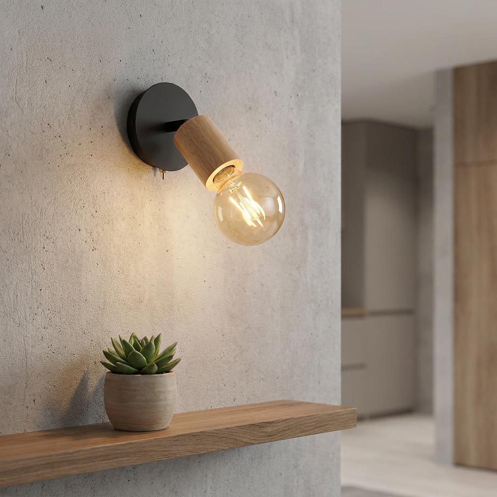 Modern black and wood wall light with a glowing filament bulb, mounted on a concrete wall above a wooden shelf.