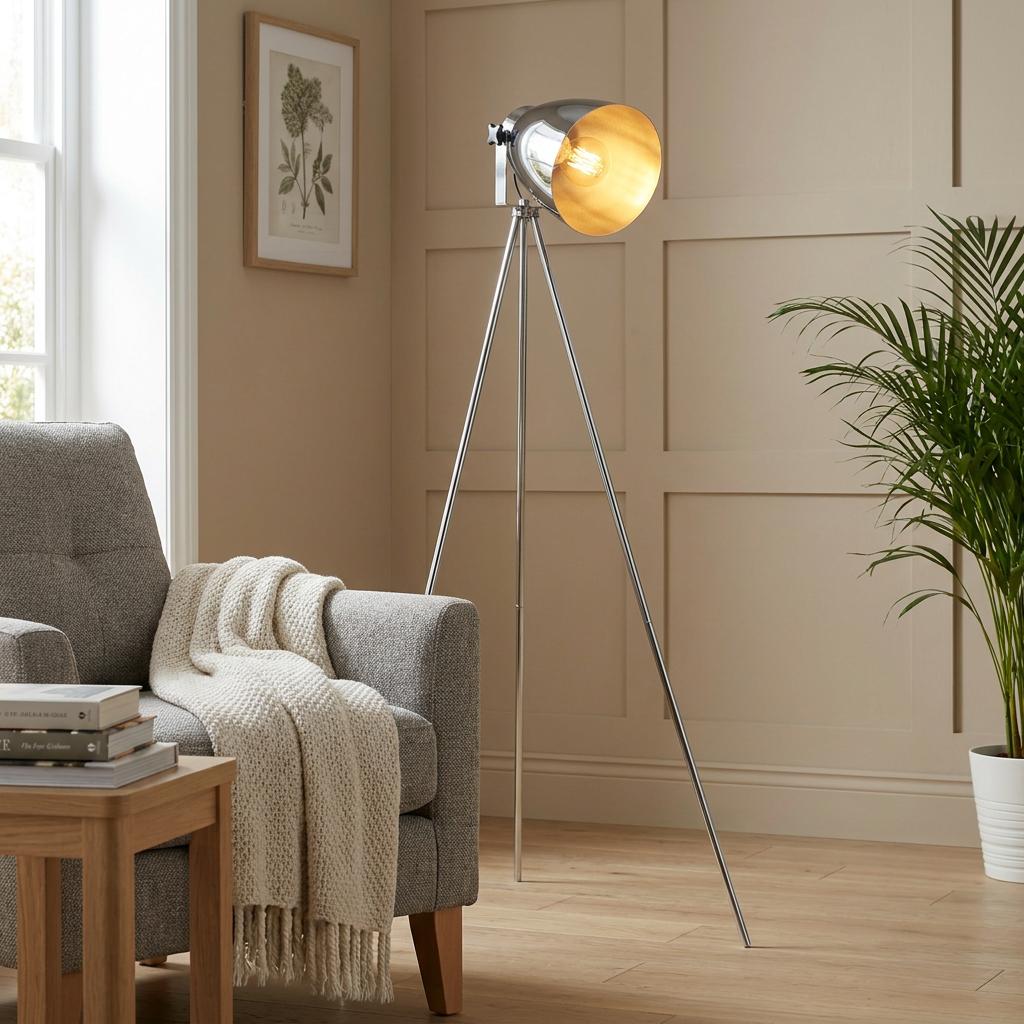 Industrial chrome tripod floor lamp with a gold interior shade glowing in a modern living room setting.