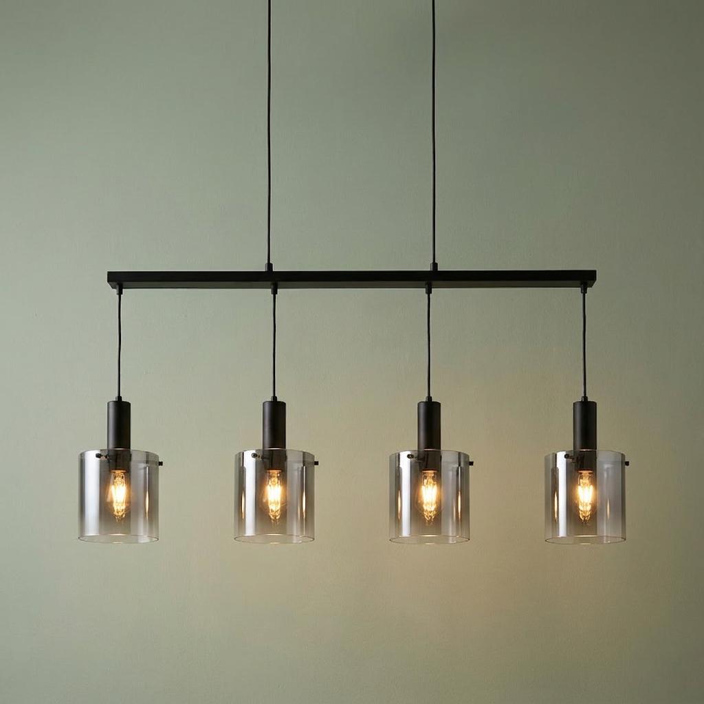 Four-light black bar pendant with smoked ombre cylinder glass shades illuminated against a green wall.