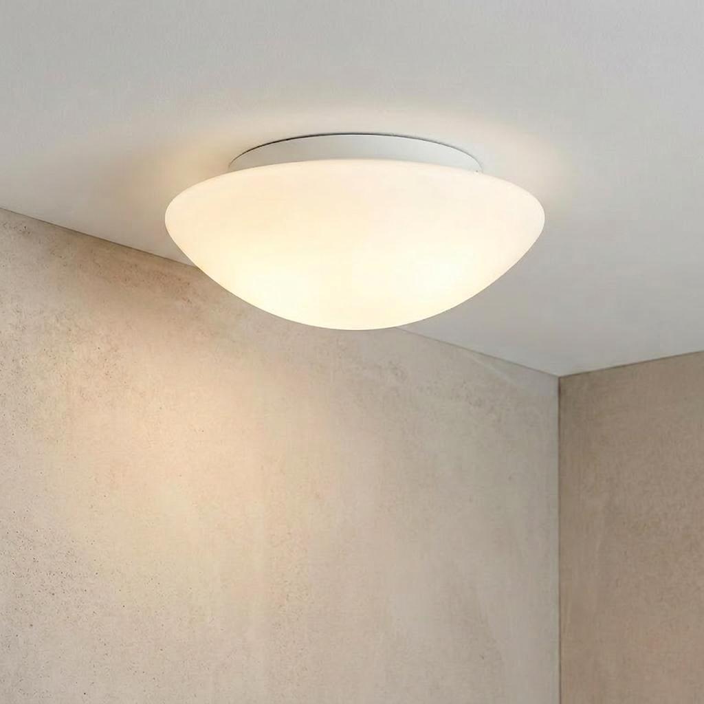 A circular opal glass flush ceiling light illuminating a minimalist room with a soft glow.