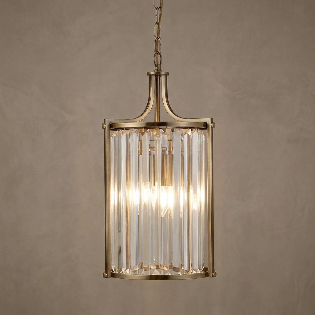 A brass pendant light featuring a cylindrical shade made of vertical crystal rods, illuminated from within.