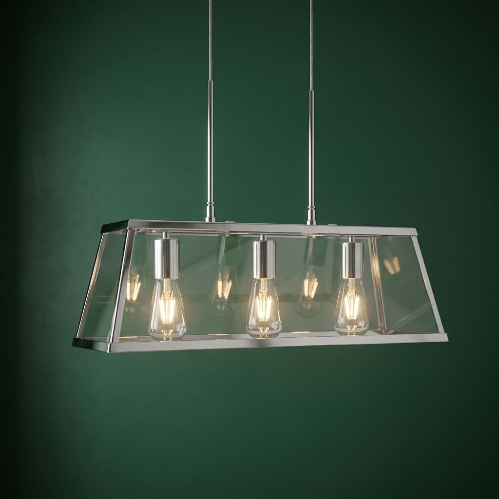 Chrome three-light lantern bar with clear glass panels and lit bulbs against a dark green wall.