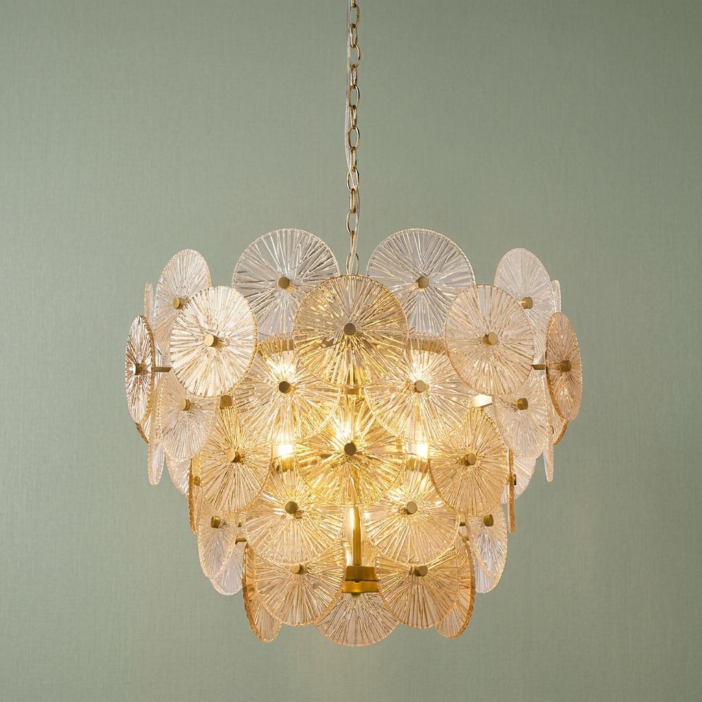 Tiered bronze chandelier with circular ribbed glass discs illuminated against a pale green wall.