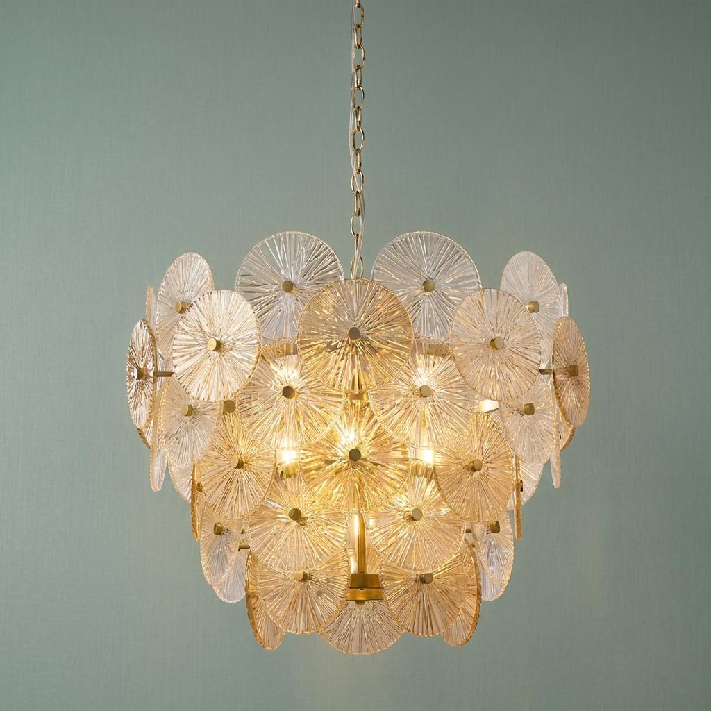 Bronze chandelier with tiered ribbed glass discs in clear and amber tones against a soft blue wall.