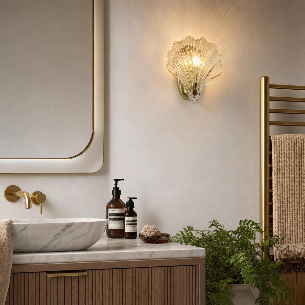 A shell-shaped amber glass wall light glowing above a marble sink and wooden vanity in a modern bathroom.