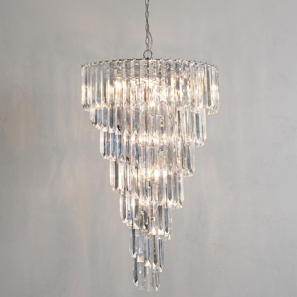 Five-tier chrome chandelier with clear acrylic rods in a tapered design, illuminated against a textured grey wall.