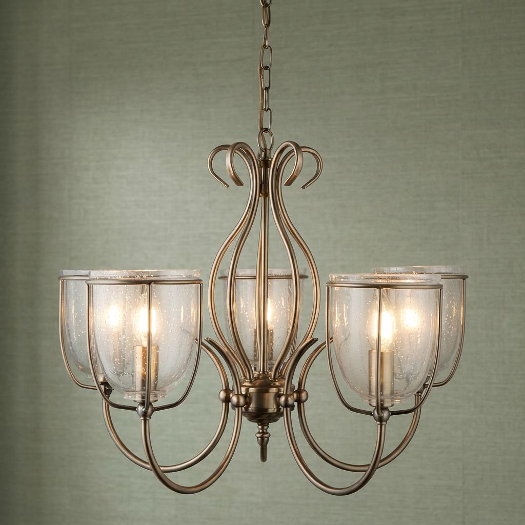 Antique brass 5-light pendant with seeded glass shades and curved metal frame against a textured green wall.