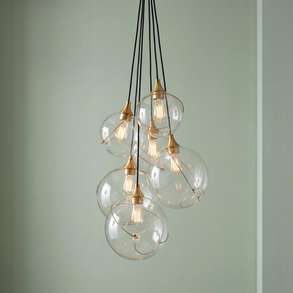 Skye 6 Light Ceiling Pendant Light with clear glass globes and brass fittings clustered against a sage wall.
