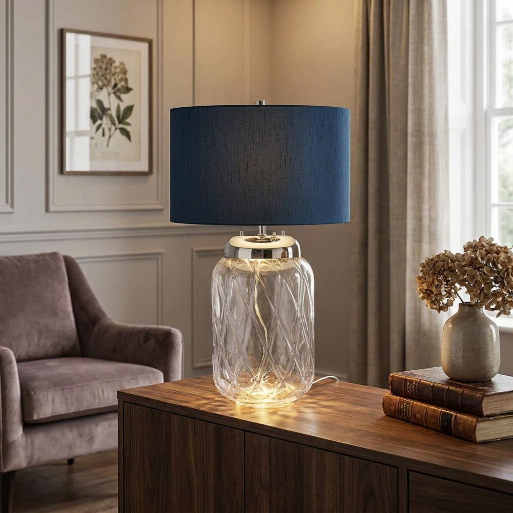 Sola 2 Light Glass Table Lamp with a navy blue drum shade and illuminated textured glass base on a sideboard.