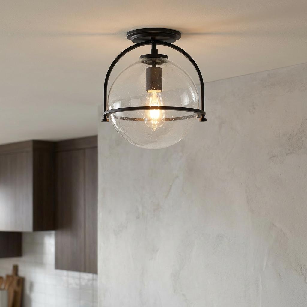 A black flush-mount ceiling light with a clear seeded glass globe and glowing Edison bulb in a modern kitchen.