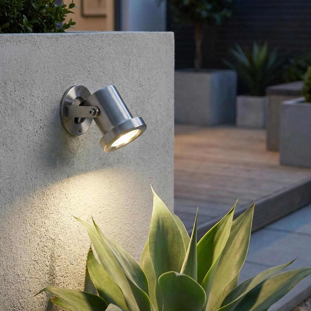 Stainless steel outdoor spotlight mounted on a concrete wall, illuminating a succulent plant in a modern garden.