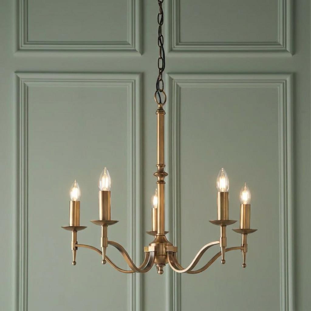 Stanford 5-light antique brass chandelier with lit candle bulbs against a green paneled wall.