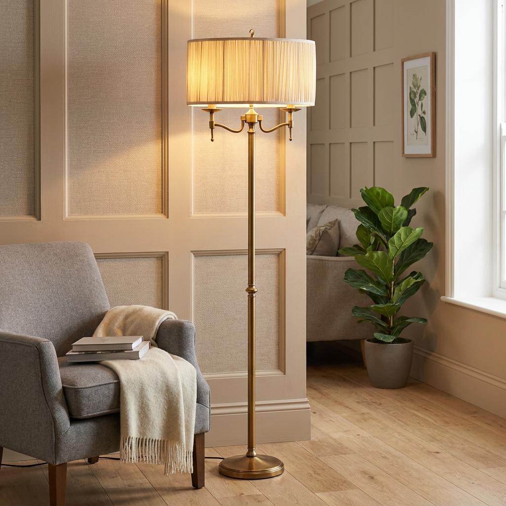 Stanford antique brass floor lamp with a pleated shade in a cozy living room next to a grey armchair.