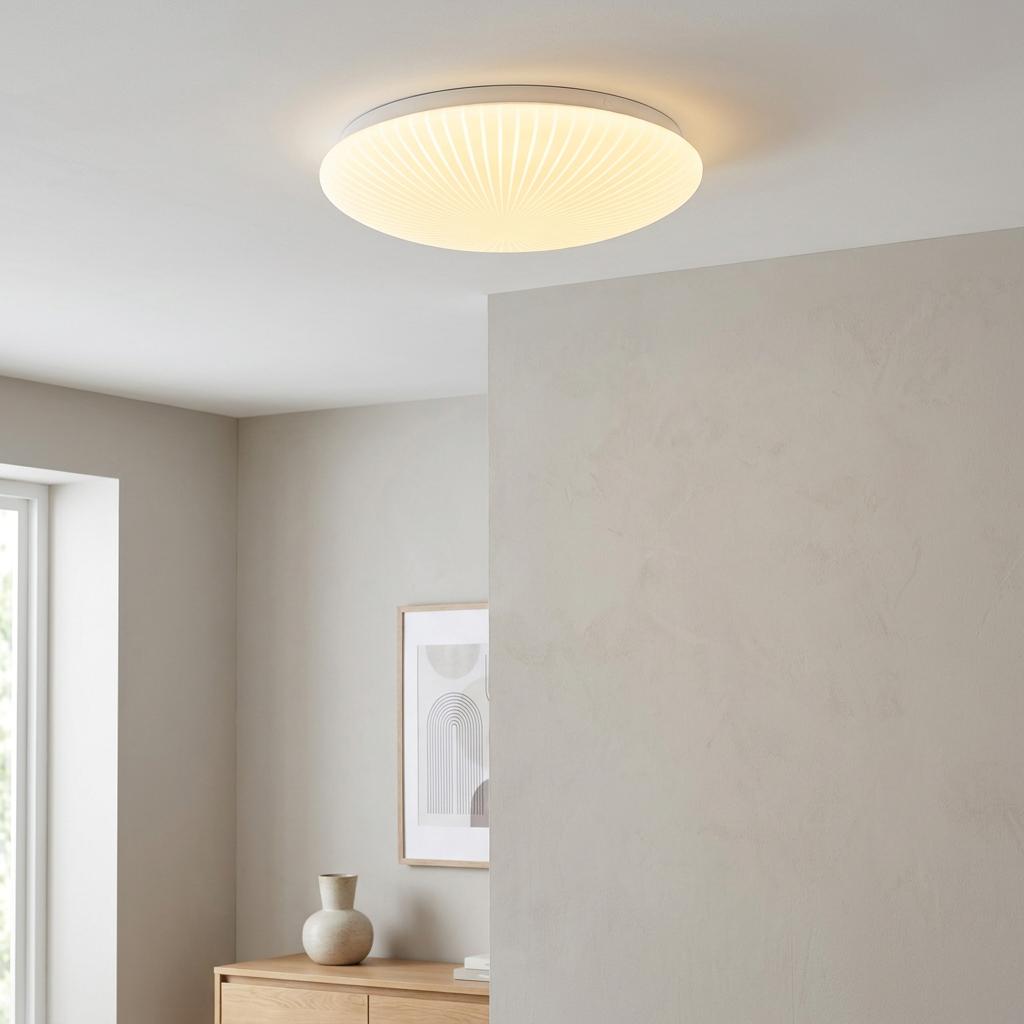 Stripy, white acrylic flush ceiling light with integrated LED illuminated on a neutral ceiling in a modern room.
