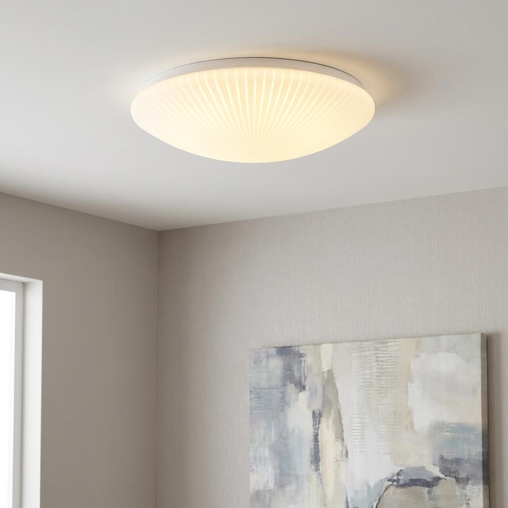 Illuminated stripy white acrylic flush mount LED ceiling light in a modern room above abstract wall art.