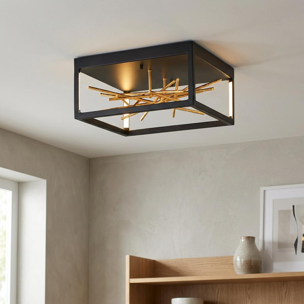 Square black flush-mount ceiling light with a gold branch detail illuminated in a modern neutral-toned room.