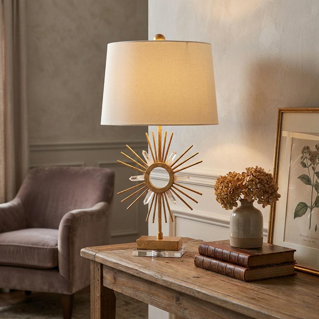 Sun King gold leaf table lamp with a sunburst base and cream shade on a wooden console table with vintage books.