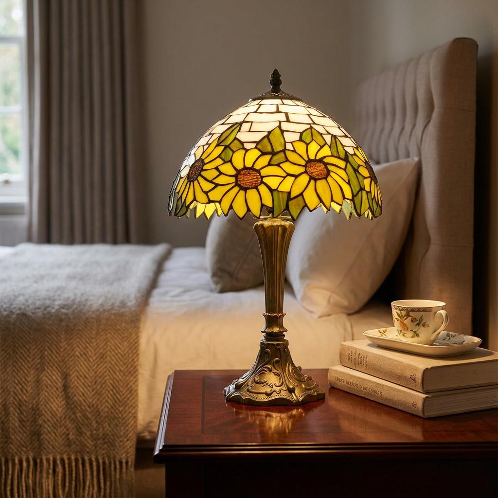 Sunflower Tiffany table lamp with a stained glass shade glowing on a wooden bedside table in a neutral bedroom.