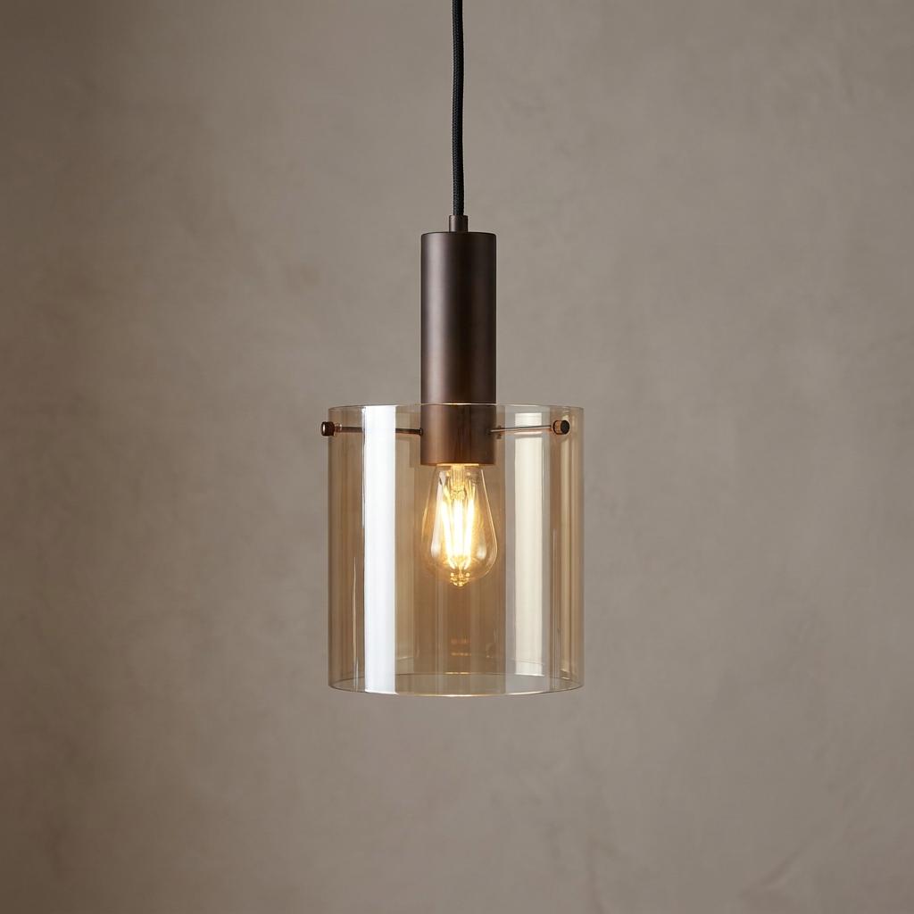 Modern pendant light featuring a cylindrical amber glass shade and dark bronze socket against a neutral wall.