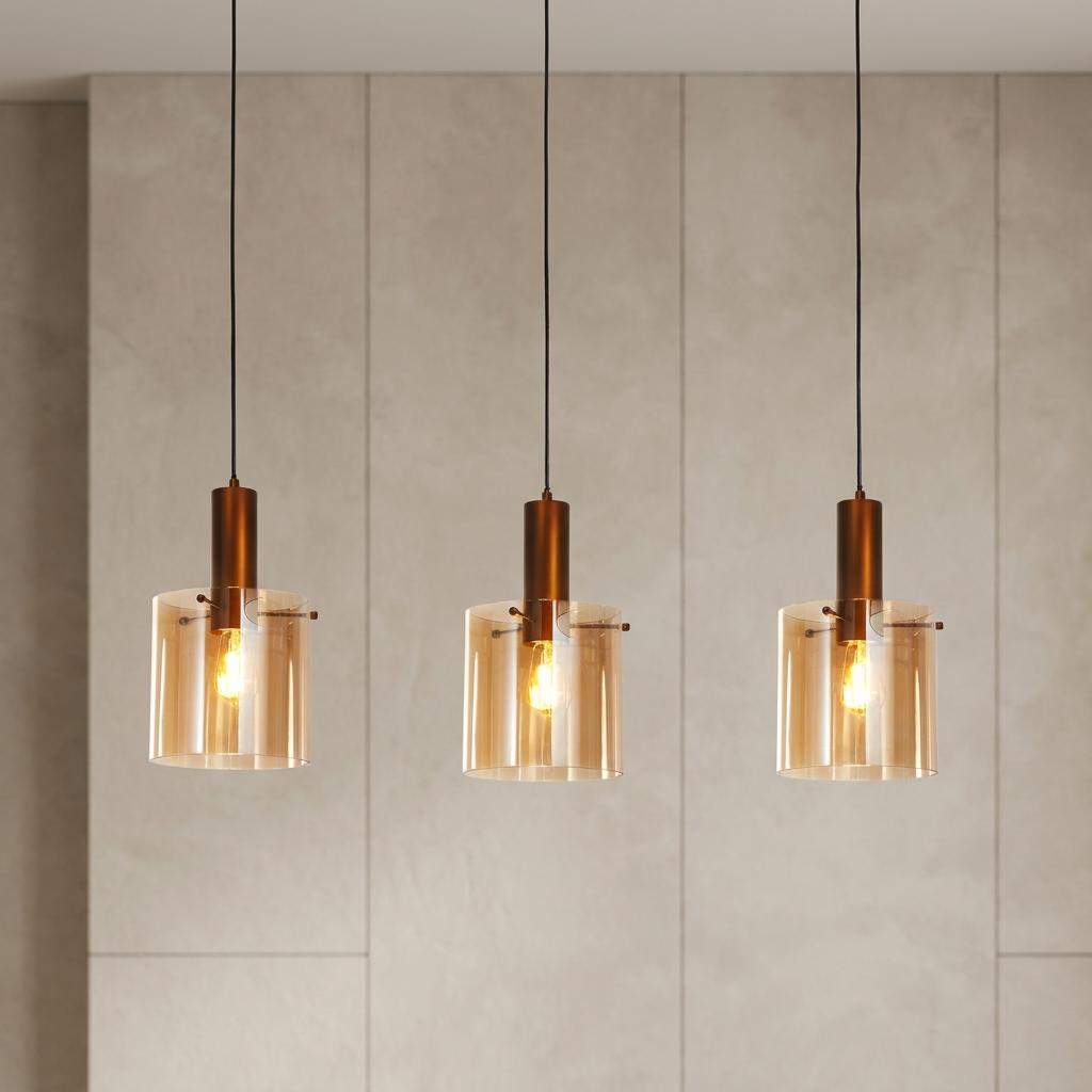 Trio of amber glass pendant lights with mocha metal fixtures glowing against a neutral panelled wall.
