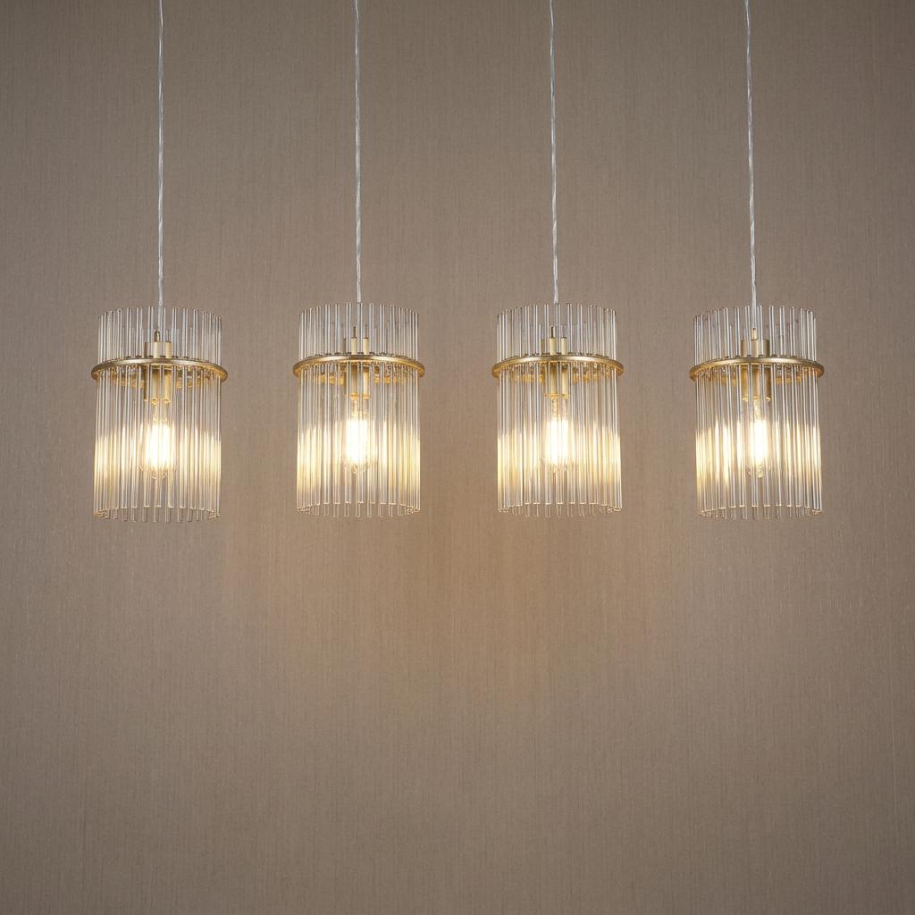 Four illuminated gold and champagne glass rod pendant lights hanging in a row against a textured wall.
