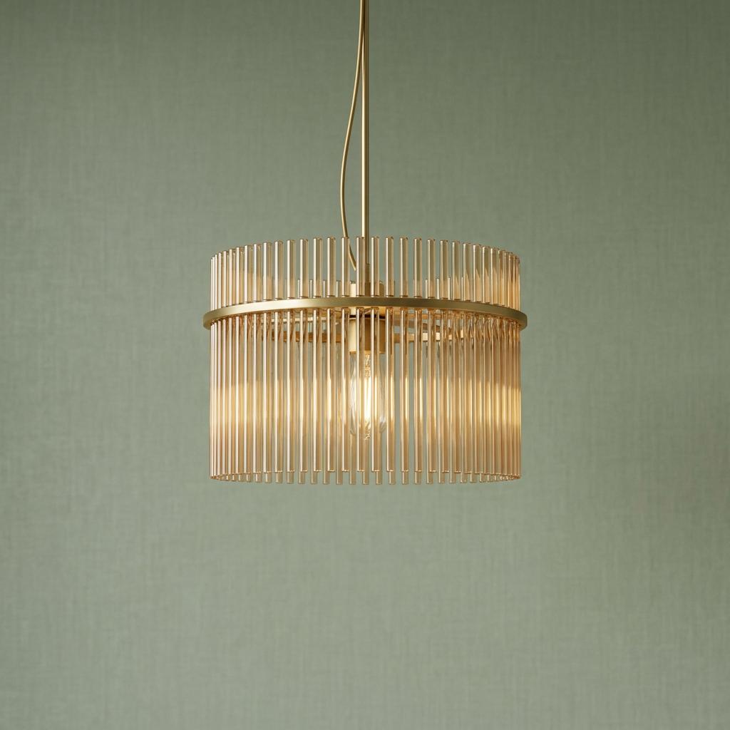 A Swizzle gold and champagne pendant light with vertical glass rods glowing against a sage green wall.