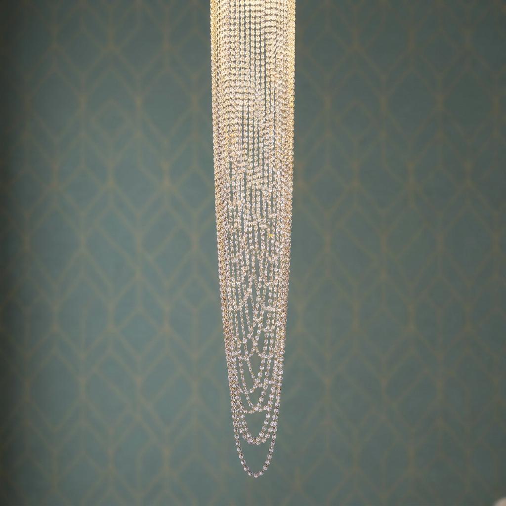 Cascading strands of clear crystals from a chandelier against a teal geometric patterned wallpaper.