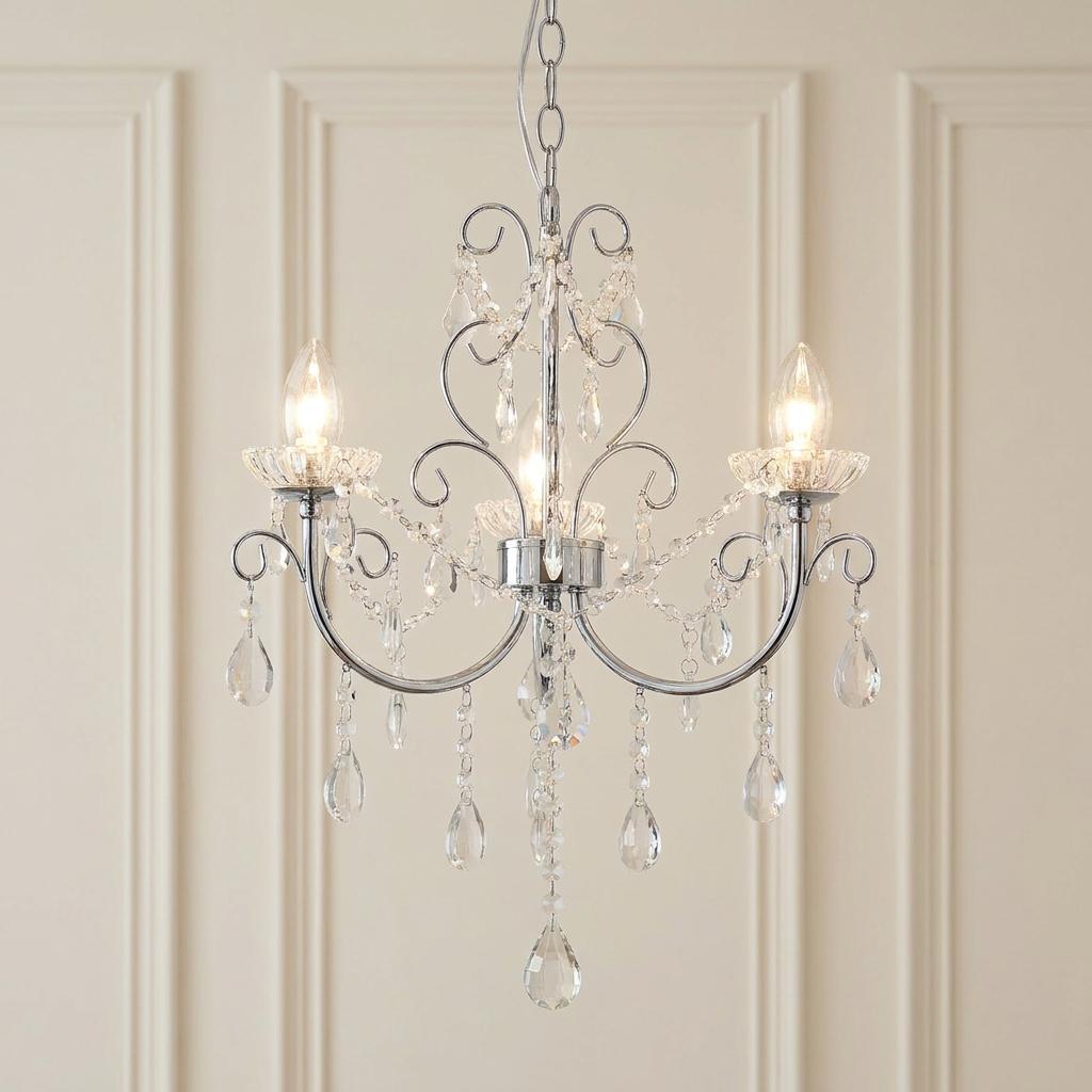 Three-light chrome chandelier with hanging crystal droplets and scrolled arms against a neutral paneled wall.
